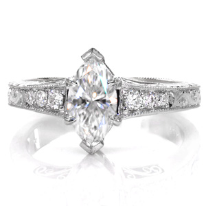 The exquisite combination of bright-cut and relief engraving styles creates a beautiful vintage engagement ring option. Shown with a marquise cut center stone, the flared band complements the length of the diamond. Hand wrought filigree curls on the sides of the piece and milgrain edging add to the antique appeal.
