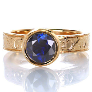 Design 3615 is shown with a sensational deep blue sapphire center stone. A modern band width and raised bezel setting add a touch of contemporary beauty while intricately hand engraved scroll patterns and milgrain edging provide a vintage appeal. The details all blend seamlessly together for a unique solitaire style. 