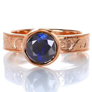 Design 3615 is shown with a sensational deep blue sapphire center stone. A modern band width and raised bezel setting add a touch of contemporary beauty while intricately hand engraved scroll patterns and milgrain edging provide a vintage appeal. The details all blend seamlessly together for a unique solitaire style. 