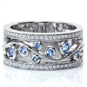 This stunning wide band design features an elegant filigree design perfect for showing off lushly colored gem stones. The pale blue sapphires shown are set in wrapping-bezels as the filigree flows between two micro pavé diamond rails. Beaded milgrain texture frames the diamonds and adds to the vintage appeal.