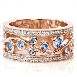 This stunning wide band design features an elegant filigree design perfect for showing off lushly colored gem stones. The pale blue sapphires shown are set in wrapping-bezels as the filigree flows between two micro pavé diamond rails. Beaded milgrain texture frames the diamonds and adds to the vintage appeal.