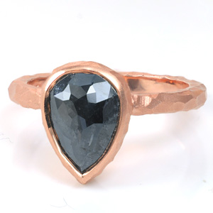 This solitaire design is shown with a pear shaped, rose cut, salt and pepper diamond. The band is hand hammered and carved to create a faceted texture that compliments the top-facets of the stone. The dark gray-black of the center stone looks stunning with any of the precious metal colors.