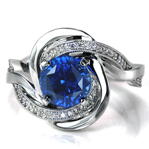 Evoking thoughts of the rippling ocean waves, Design 3651 features intertwining bands that flow around the blue sapphire center stone to form a unique halo. The contrast between the diamond set band and the high polished band adds to the motion of the piece. 