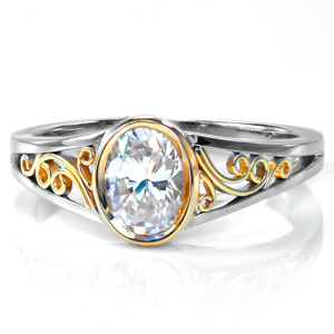 This stunning two-tone design mixes modern sleekness with vintage elegance. The bezel style center setting and the hand wrought filigree curls are shown in 18k yellow gold with a white split shank band style. The low height of the setting allows for easy wear.