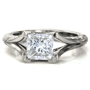 This is a beautifully geometric piece with antique detailing. Shown with a princess cut center stone, the side views feature matching princess cut surprise diamonds in bezel settings. The filigree to the sides of the surprise stones is hand crafted. Hand engraved scroll patterns and milgrain edging complete the look. 