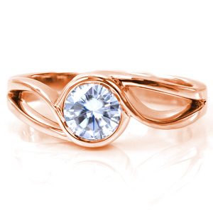 This contemporary solitaire design has a flowing band that bypasses the diamond to form an elegant bezel setting. The band features a split shank style to add width and movement to the piece. The mesmerizing twist will keep all eyes on your center stone! 