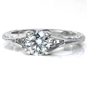 This delicate, antique inspired design features a 0.50 carat center stone in a unique four prong setting. The knife edge band features relief style engraving and milgrain edging. Hand wrought filigree curls are visible from the top and the sides of this lovely ring.