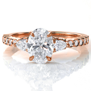 A 1.0 carat oval diamond is flanked by two pear shaped diamonds in Design 3707. The unique band features bezel set round diamonds and a high polish finish. A glamorous five petal diamond detail adds extra sparkle and flair under the custom center setting. 