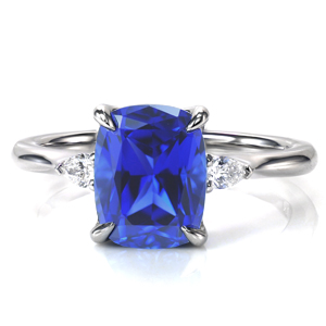 A brilliant blue 2.70 carat cushion cut sapphire is the star of this stunning design. The center stone is set in a classic four prong setting accented by sparkling, pear cut diamonds on each side. A simple, high polish band tapers slightly into the center, drawing the eye to the dazzling center. 