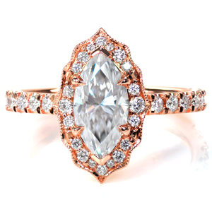 A 1.0 carat marquise diamond is framed with a vintage inspired, scalloped halo adorned with different sizes of round brilliant diamonds. The band features diamonds set in a delicate, French pave style, and the cathedral style shoulders arch gracefully up to touch the base of the halo. 