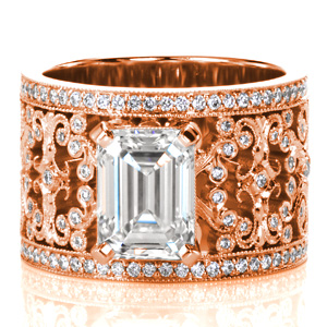 Design 3755 is a stunning example of sophisticated artistry. A 2 carat emerald cut diamond is set atop the intricately detailed wide band. Broad filigree flourishes curl and hold bezel set round diamonds. Each turn of metal has hand applied milgrain detail for a vintage look. Rows of bead set diamonds frame the band. 