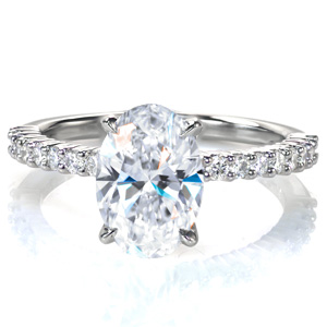 A 2 carat oval is set simply atop a charming shared prong band with round brilliant diamonds spanning half way around the ring. This classic style delivers lots of sparkle, and it is designed so that any wedding band design will sit flush against it. 
