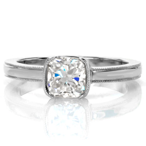 This 1 carat cushion cut diamond is surrounded by an elegant 14k white gold half bezel setting, allowing a lovely profile view of the stone. The band and bezel are outlined with milgrain detail to add a delicate texture and shape to the edges. The glow of the high polish band compliments the dazzling diamond center.