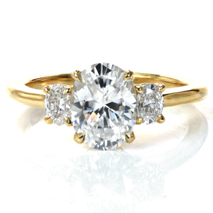 Our Charlotte design is a classic three stone engagement ring with a modern update. A 1.5 carat oval diamond is flanked by oval diamonds on each side creating a perfectly symmetric look. The simple basket setting provides a clean look, and the high polish of the band complements the brilliant diamonds beautifully.
