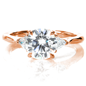 A modern take on the classic three stone engagement ring, Ava frames a 1.2 carat center diamond with two trillion shaped side stones. The elegant curves of the basket setting flow perfectly into the high polished tapered band, drawing your eyes toward the stunning diamonds. 