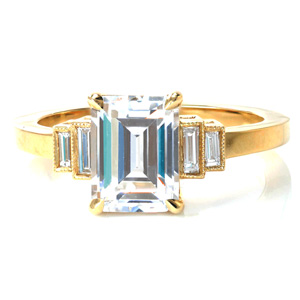 Timeless elegance is the hallmark of our Napier design. A stunning emerald cut center stone is held in four claw prongs. Bezel set baguette side diamonds step down from the center stone into a high polished band. Hand applied milgrain detail outlines the side diamonds for just a touch on vintage flair. 