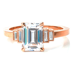 Timeless elegance is the hallmark of our Napier design. A stunning emerald cut center stone is held in four claw prongs. Bezel set baguette side diamonds step down from the center stone into a high polished band. Hand applied milgrain detail outlines the side diamonds for just a touch of vintage flair. 