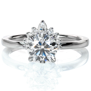Like a solitaire wearing a tiara, Design 3789 sparkles from every angle. A 1 carat round brilliant diamond is held in a classic four prong setting atop a delicate, rounded band. One side of the center diamond is adorned with eight small round diamonds and one pear shaped diamond, creating a half halo. 