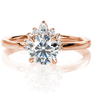 Like a solitaire wearing a tiara, Design 3789 sparkles from every angle. A 1 carat round brilliant diamond is held in a classic four prong setting atop a delicate, rounded band. One side of the center diamond is adorned with eight small round diamonds and one pear shaped diamond, creating a half halo. 