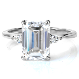 A stunning 2 carat emerald cut diamond is cradled in a delicate, draped basket setting with four small claw prongs. Flanking the center stone are two small pear shaped diamonds, adding brilliant sparkle and a lovely contrast. The delicate, high polished band tapers in slightly to meet the points of the pears. 