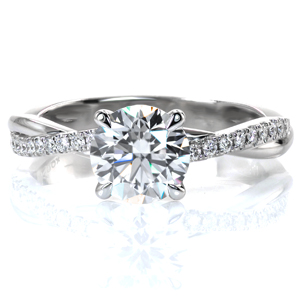 A glimmering 1 carat round brilliant diamond is showcased in a classic four prong setting. The narrow band intertwines, mixing a row of hand set diamonds and a row of high polished metal, adding texture and interest. This updated twist on a classic ring sparkles and shines from every angle. 