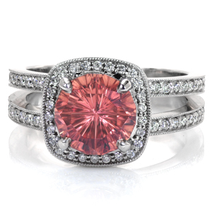 A stunning 3 carat peachy pink sapphire is surrounded by a cushion shaped halo of glimmering diamonds. More diamonds accent the split shank band for sparkle from every direction. Elegant hand applied milgrain texture frames the diamonds on the ring and adds a vintage nod to this striking design. 