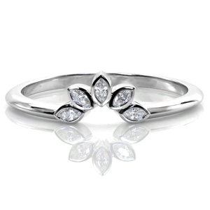 A delicate band engineered to curve around the center stone of an engagement ring, this design features five bezel set marquise diamonds arranged to look like brilliant, sparkly flower petals. The thin, polished band leading into the diamonds is the perfect complement to just about any solitaire. 