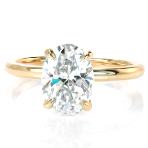 A dazzling oval diamond is simply showcased in an elegant four prong setting. A decorative basket adds a bit of extra sparkle and flair and gives the profile view added interest. Set in warm yellow gold, this classic solitaire is a timeless statement of elegance and grace.