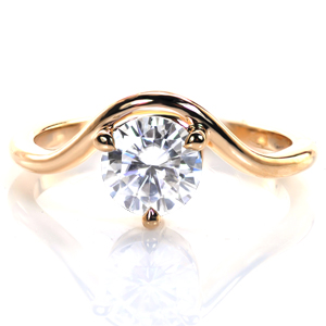 Sleek, understated, and modern, this design is an exercise in elegant restraint. A classic 1 carat round brilliant diamond is held in a unique three-prong setting that sits just atop the finger. A thin, polished band completes this design by gently curving around the stone. 