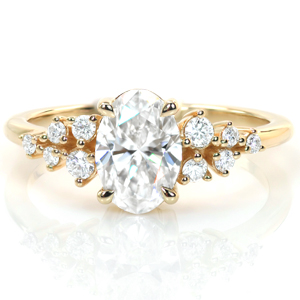 Dainty and delicate, this design features a gorgeous 1 carat oval diamond in a low, four-prong setting. Clusters of round diamonds flank the center stone with more sparkle and add to the whimsical feel of this vintage inspired engagement ring. A thin polished band completes this lovely ring. 