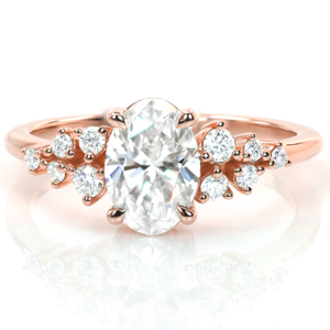 Dainty and delicate, this design features a gorgeous 1 carat oval diamond in a low, four-prong setting. Clusters of round diamonds flank the center stone with more sparkle and add to the whimsical feel of this vintage inspired engagement ring. A thin polished band completes this lovely ring. 