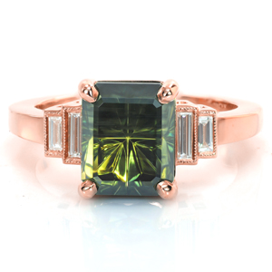 Timeless elegance is the hallmark of this design. A uniquely cut green sapphire is held in four rounded prongs. Bezel set baguette side diamonds step down from the center stone into a high polished band. Hand applied milgrain detail outlines the side diamonds for just a touch of vintage flair.