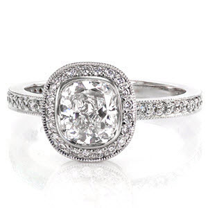 Simple elegance is brought to light with this design; featuring a 1.20 carat cushion cut center diamond in a bezel setting. The halo and delicate band of the ring are detailed in micro pavé, adding an alluring radiance. The edges of the band and halo are detailed with milgrain to add texture.