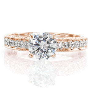 The Adorable design is simply charming! A .80 carat round center diamond is accented by bead-set side stones on the top of the band. The sides feature bezel set diamonds and cut outs, including a heart shape on the side of the center stone. All the edges are detailed in milgrain to add texture. 