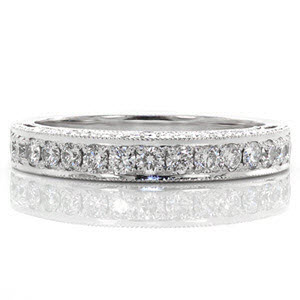 This vintage inspired band has a high side profile to allow for the pierced elements that create its pattern. The bezel set diamonds on the sides of the band are each surrounded by a curl of gold. Round diamonds accent the top of this unique wedding band. Edges are textured with milgrain to enhance its brilliance. 